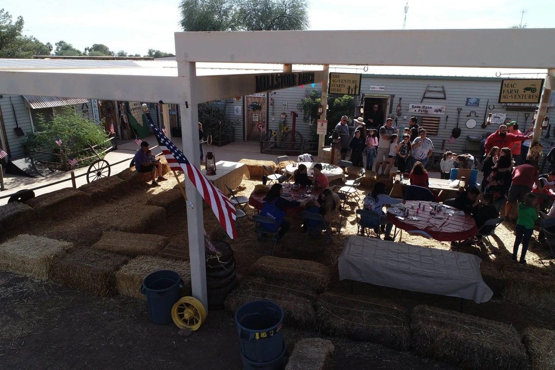 families sitting at tables with young childer under povillion with floor covred in hay.
